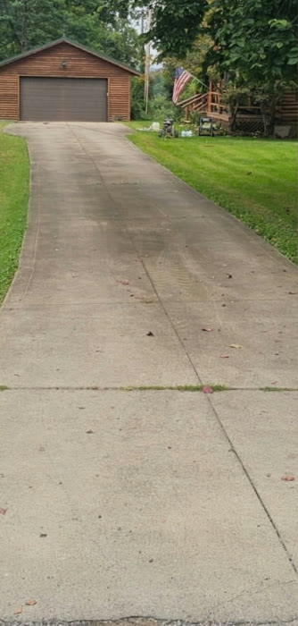 Long concrete driveway leading to a log garage, darkened with dirt and stains before cleaning